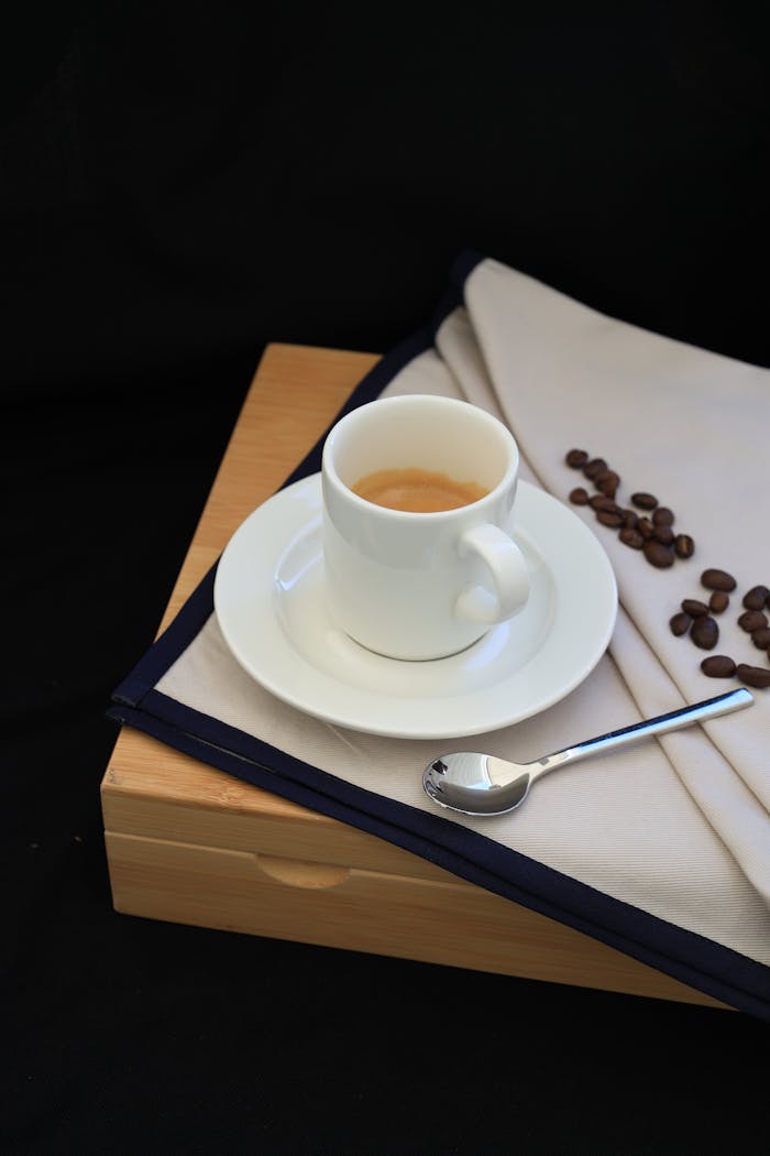 A stylish espresso cup with saucer, spoon, and coffee beans on a cloth in a minimalist setting.
